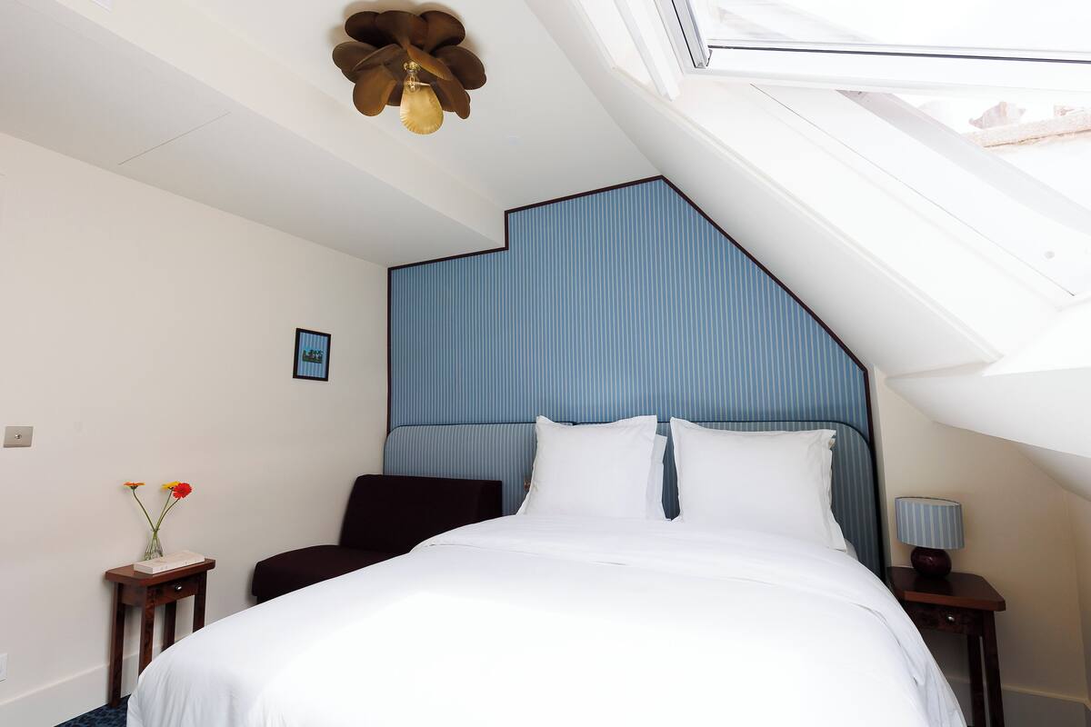 A bedroom with a bed, a nightstand, a lamp, a vase with flowers, and a ceiling fan.