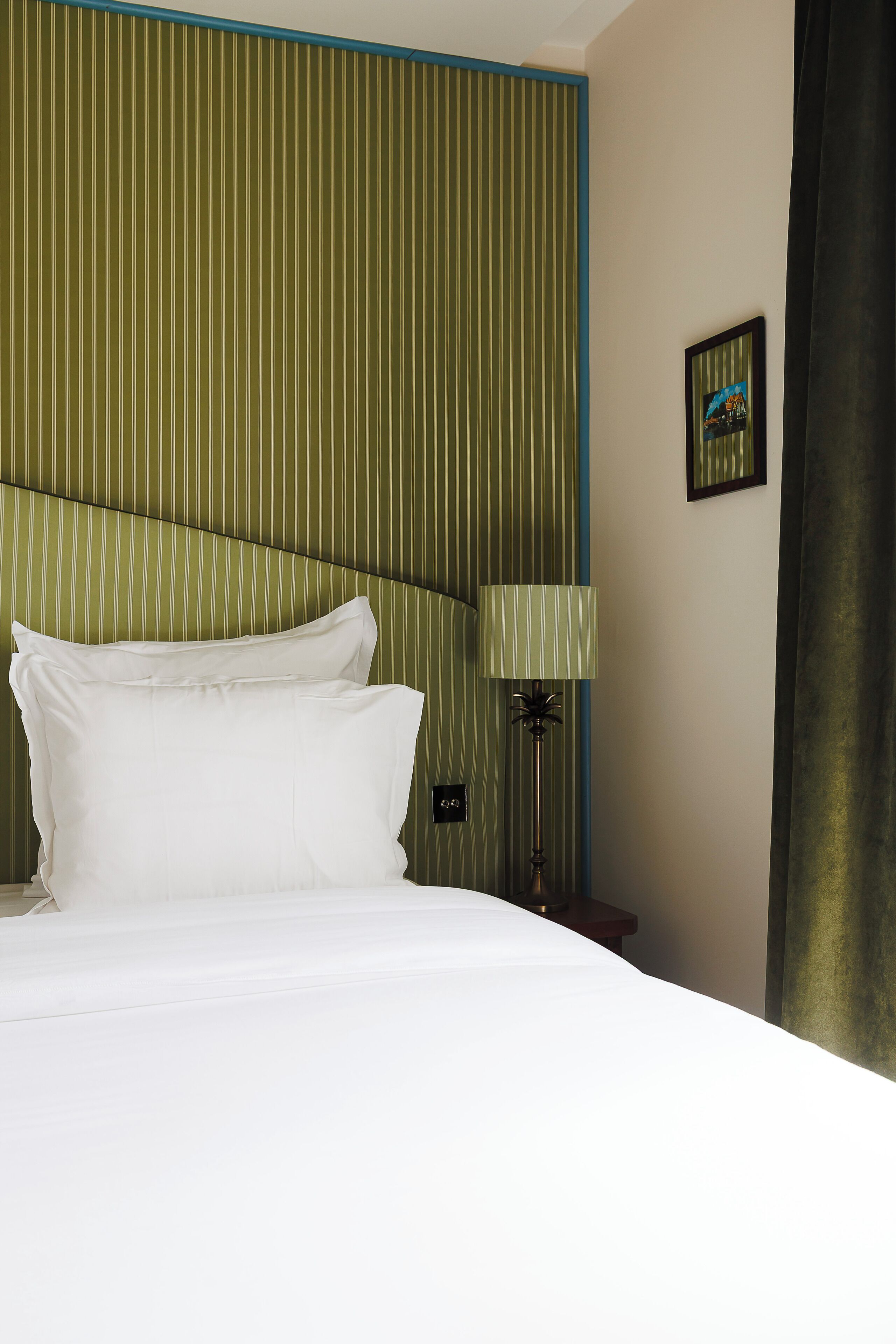 A hotel room with a bed, a nightstand, a lamp, and a framed picture on the wall.