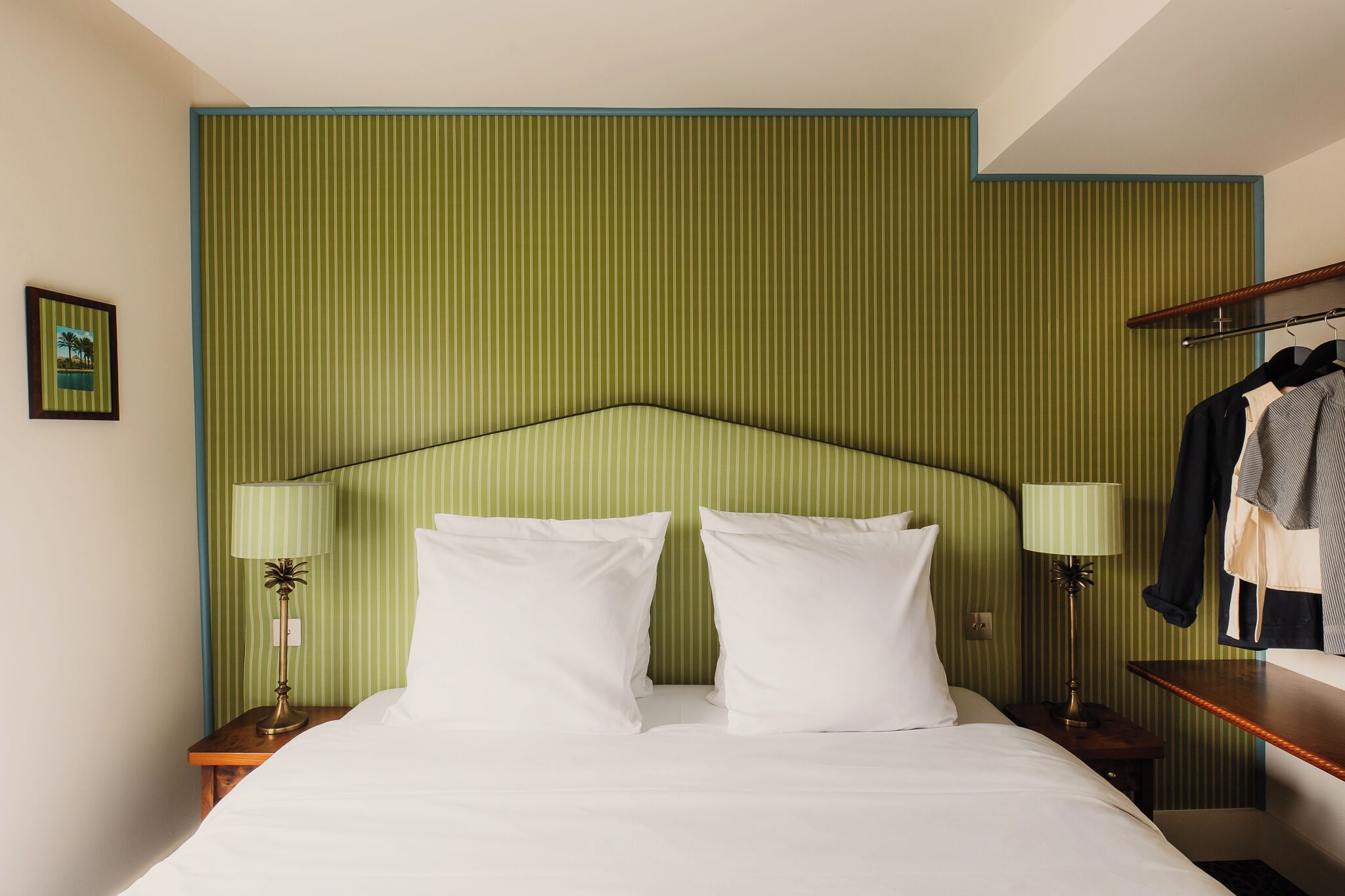 A hotel room with a bed, two bedside lamps, a nightstand, and a wooden bench.