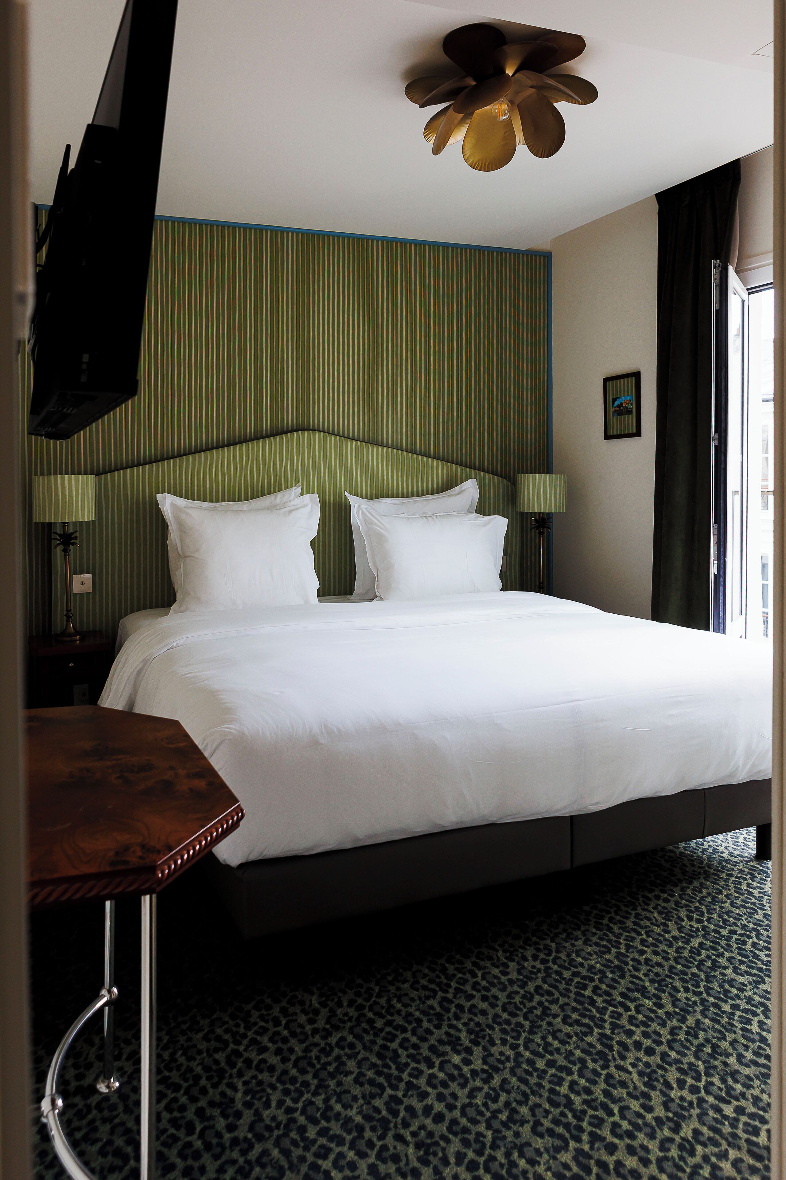 A hotel room with a large bed, a desk, a television, and a ceiling fan.