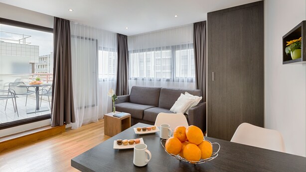 A modern living room with a sofa, dining table, and a view of the city. - Citadines Austerlitz Paris (Paris)