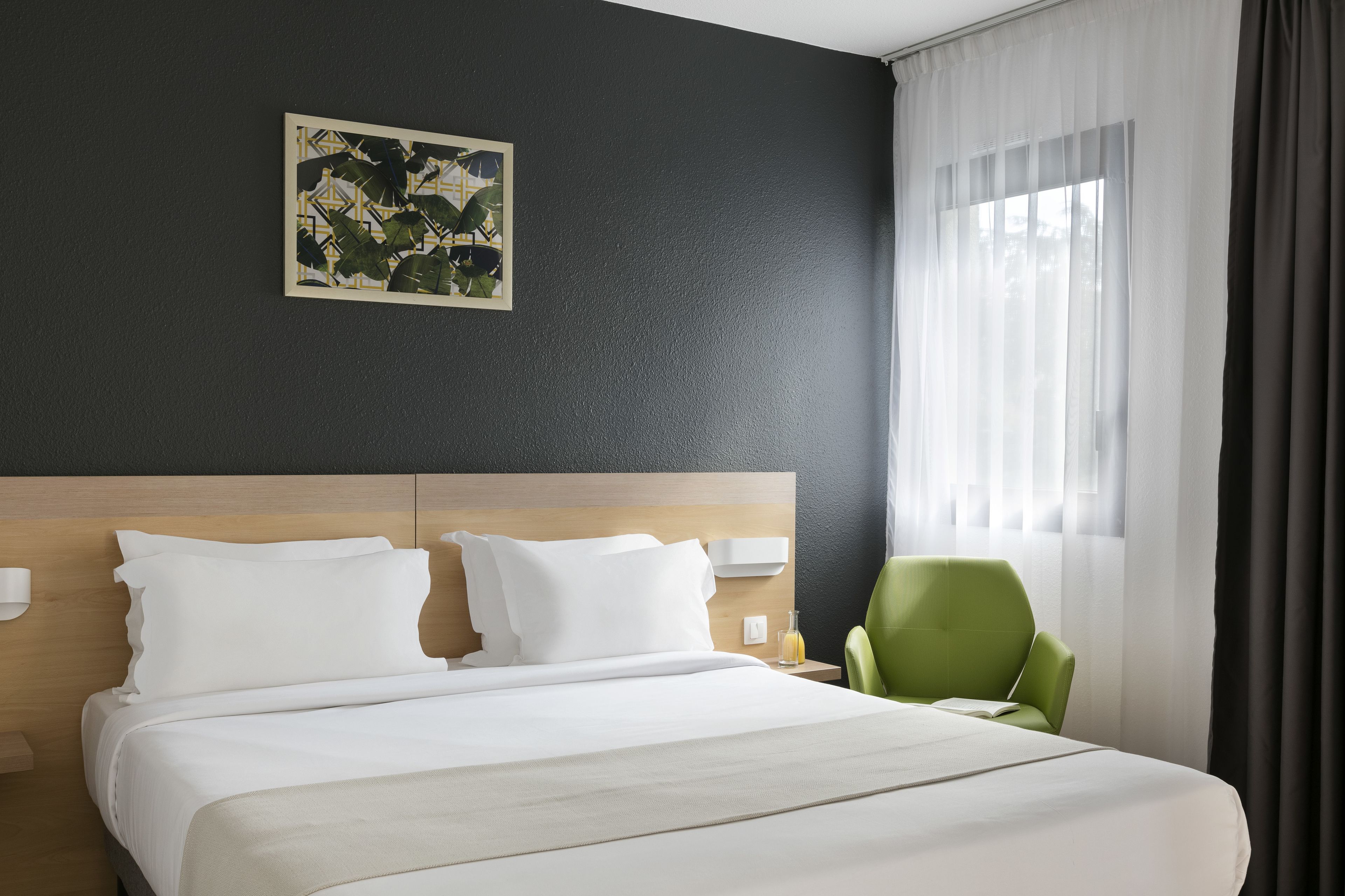 Habitación de hotel con una cama grande, una silla verde, una mesita de noche y una obra de arte colgada en la pared.