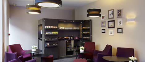 A modern lounge area with purple seating, a coffee station, and a bookshelf with various items.