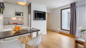 A modern kitchen with white cabinets, a microwave, and a dining area with a table and chairs. - Citadines Austerlitz Paris (Paris)