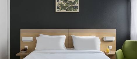 Una habitación de hotel moderna con una cama grande, dos mesitas de noche, un sillón verde y una obra de arte colgada en la pared.