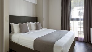 Moderni hotellihuone, jossa on suuri sänky, vaatekaappi ja näkymä ulos.