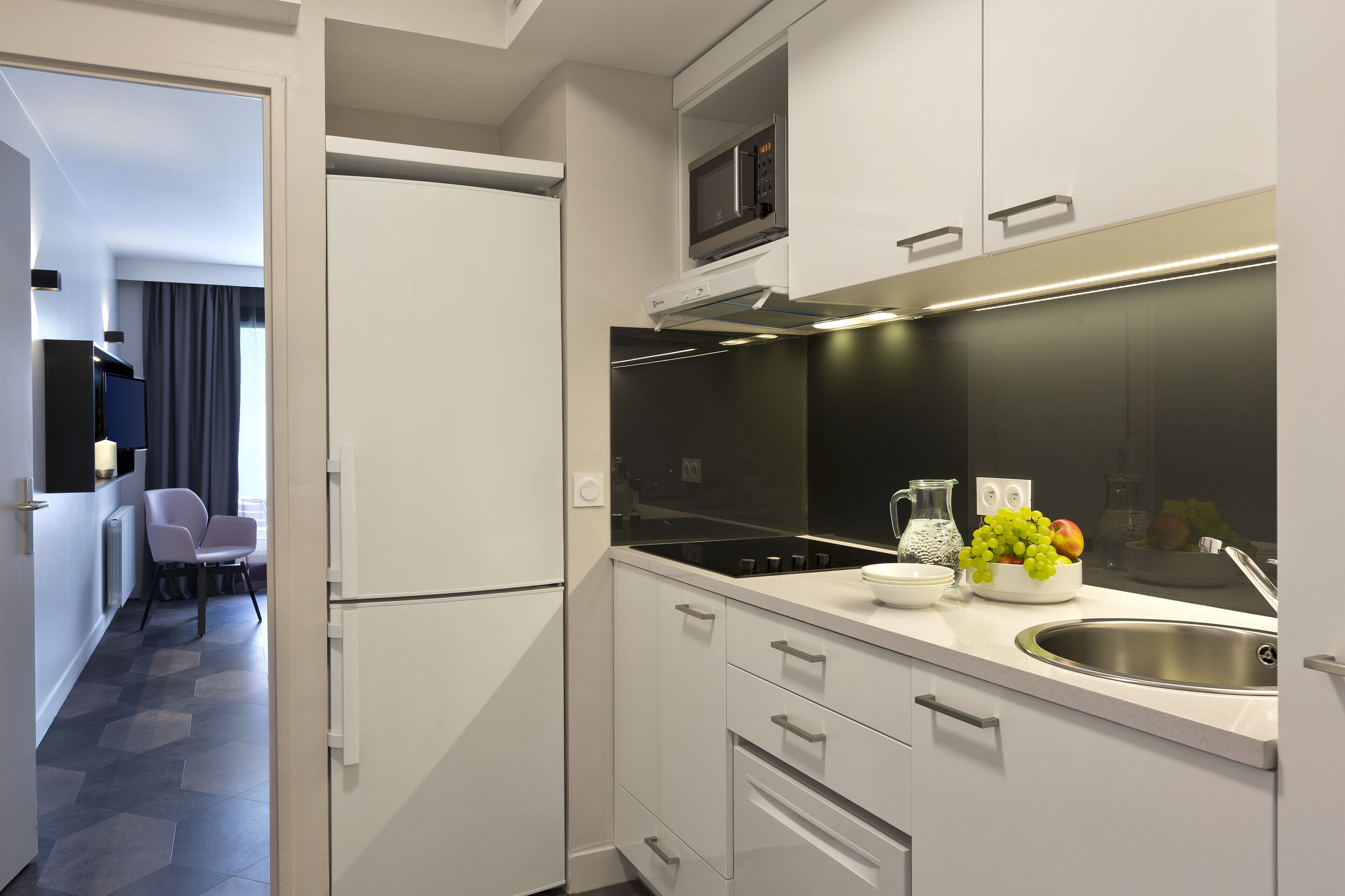 A modern kitchen with white cabinets, a built-in microwave, and a stainless steel sink.
