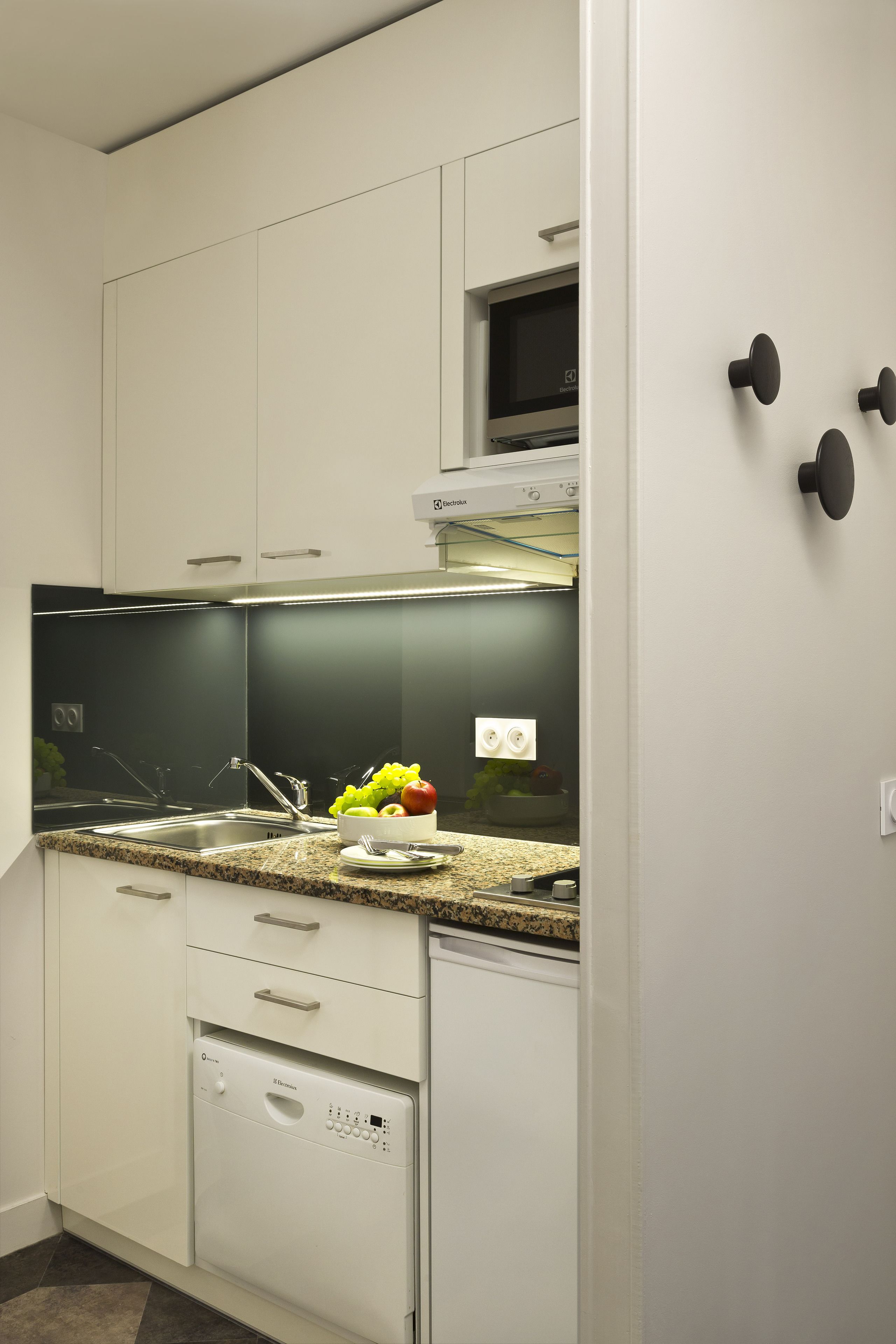 A modern kitchen with white cabinets, a granite countertop, a built-in microwave, and a dishwasher.