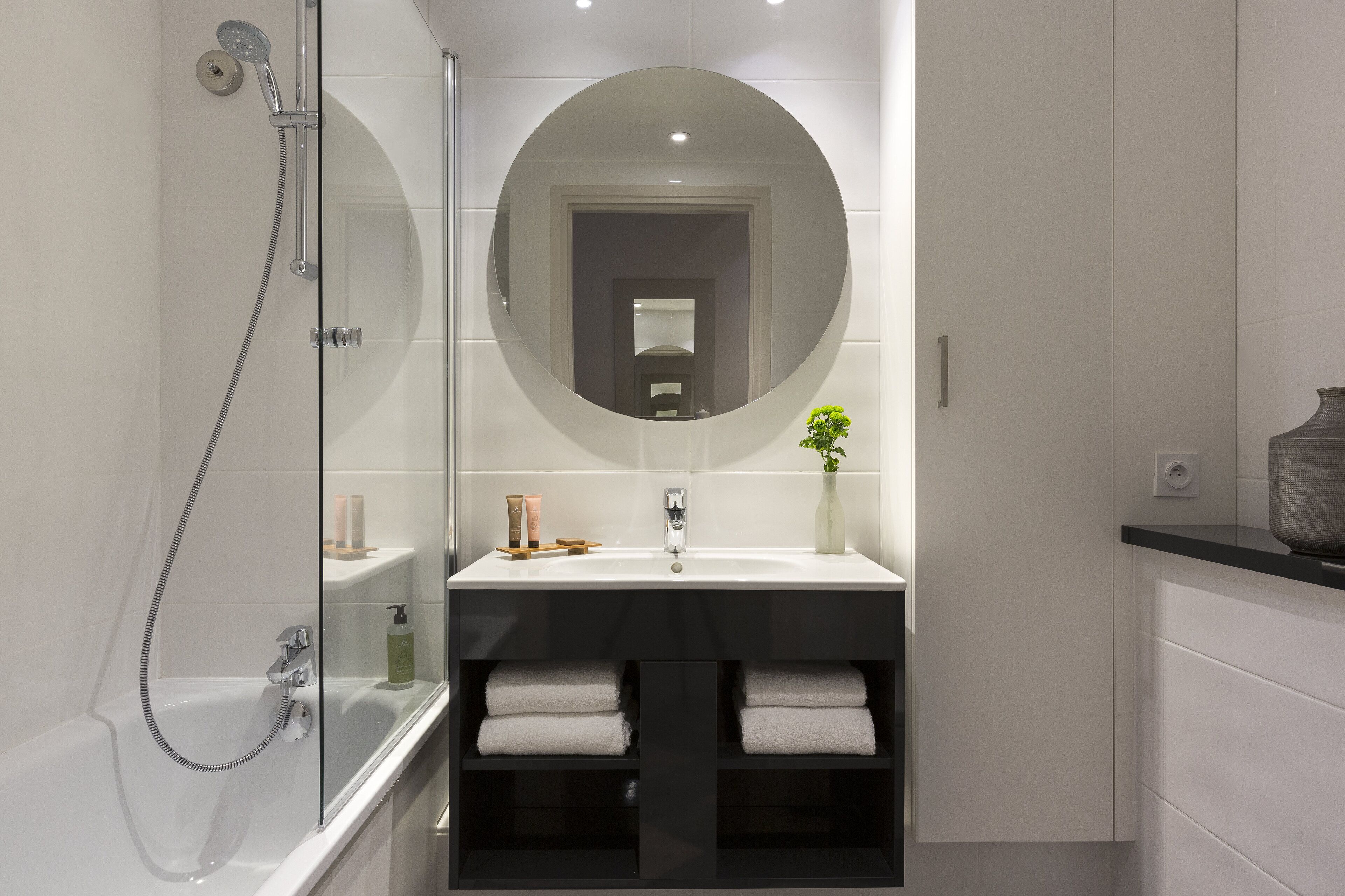 A modern bathroom with a glass-enclosed shower, a large mirror, and a vanity with a sink and towel storage.