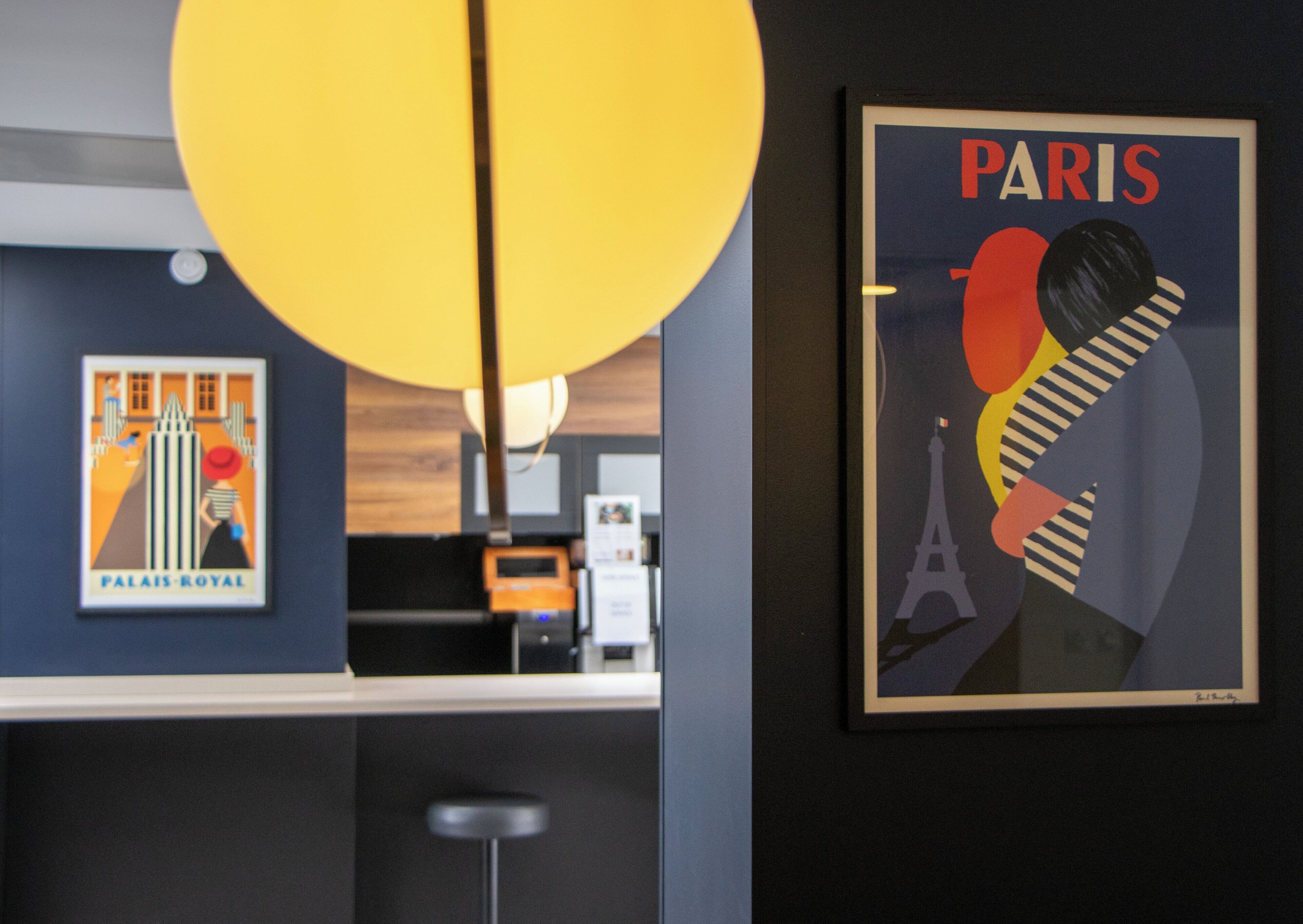 Un interior moderno con una zona de bar, una obra de arte con temática de París enmarcada y una lámpara colgante amarilla.