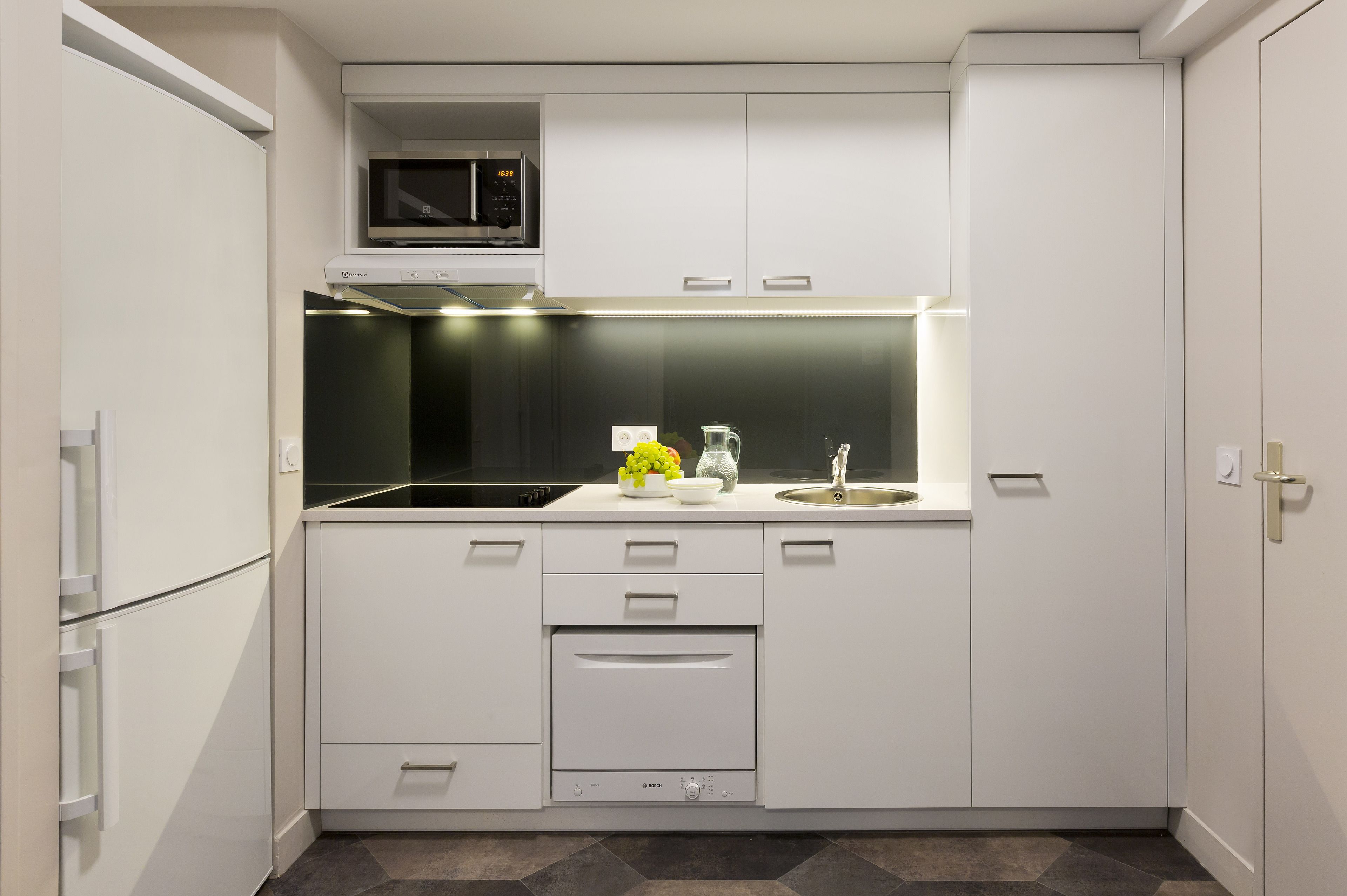 Una cocina moderna con armarios blancos, microondas integrado, lavavajillas y un fregadero.