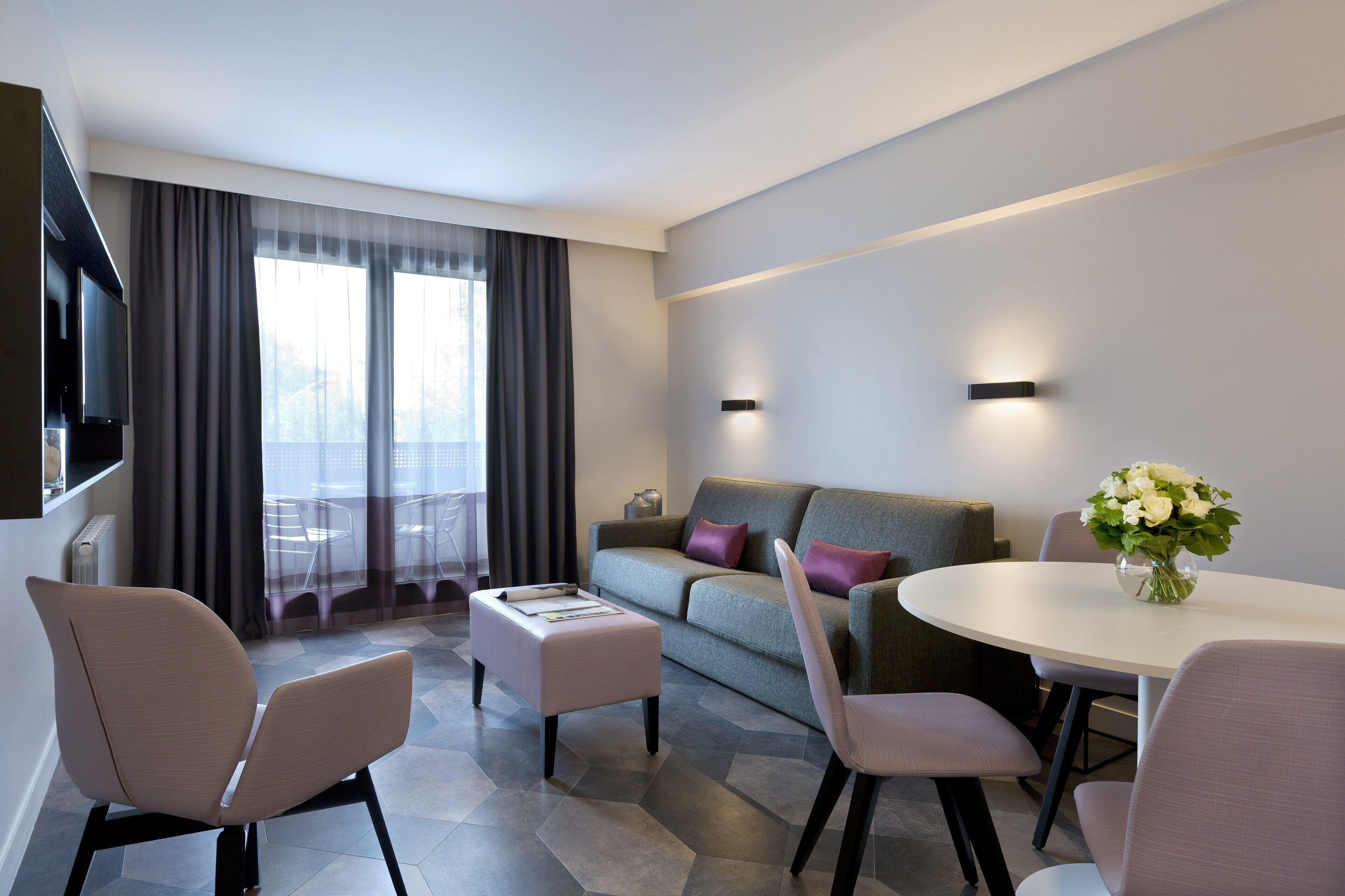 A modern hotel room with a sofa, two chairs, a small table, and a TV.