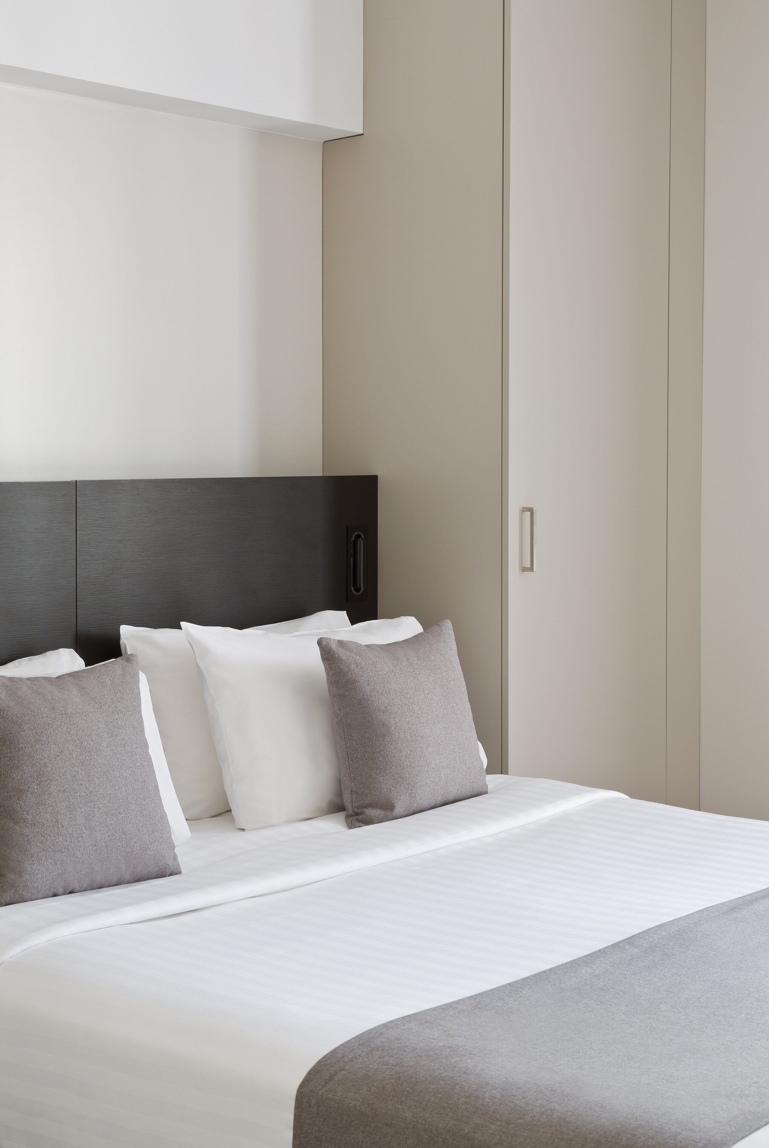 A hotel room with a bed, pillows, a headboard, and a wardrobe.