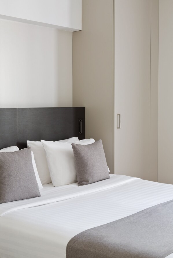 Una habitación de hotel con cama, almohadas, cabecero y armario.