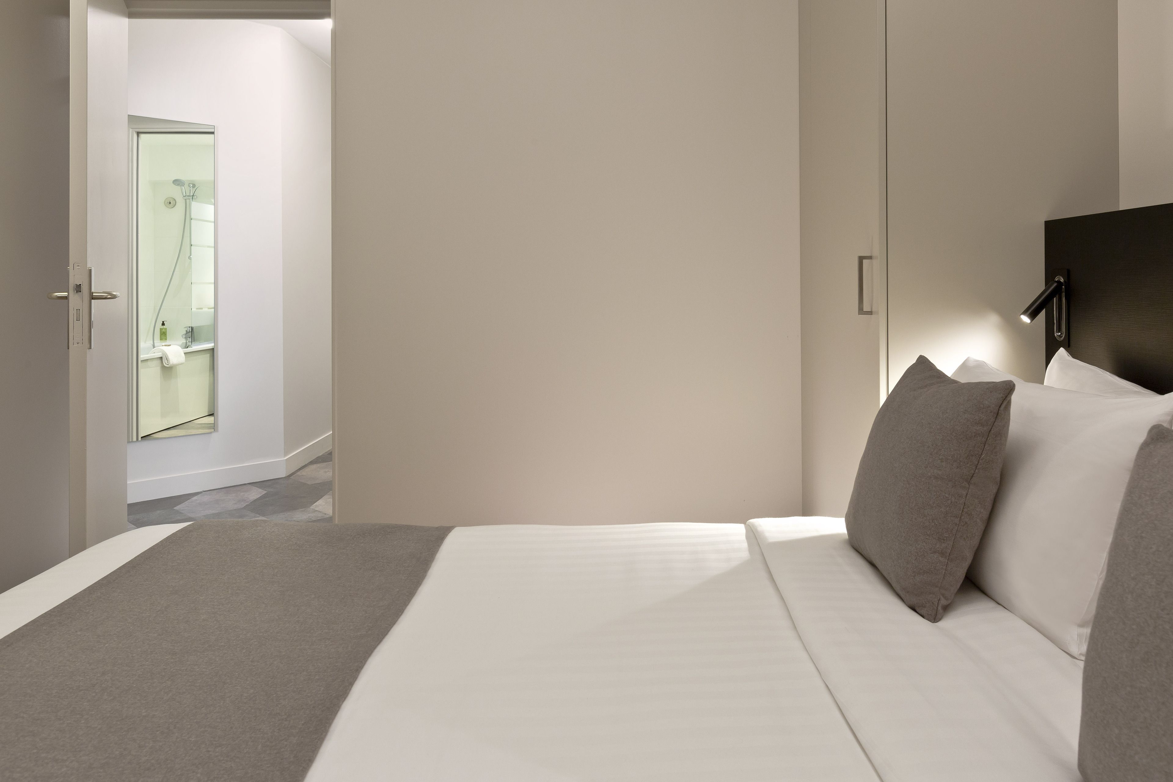 A modern hotel room with a bed, a nightstand, and a bathroom visible through an open door.