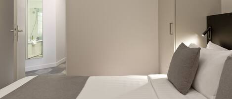 A modern hotel room with a bed, a nightstand, and a bathroom visible through an open door.