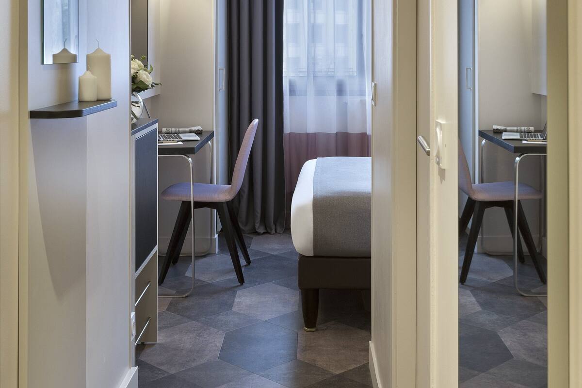 A hotel room with a bed, two chairs, a desk, and a computer.