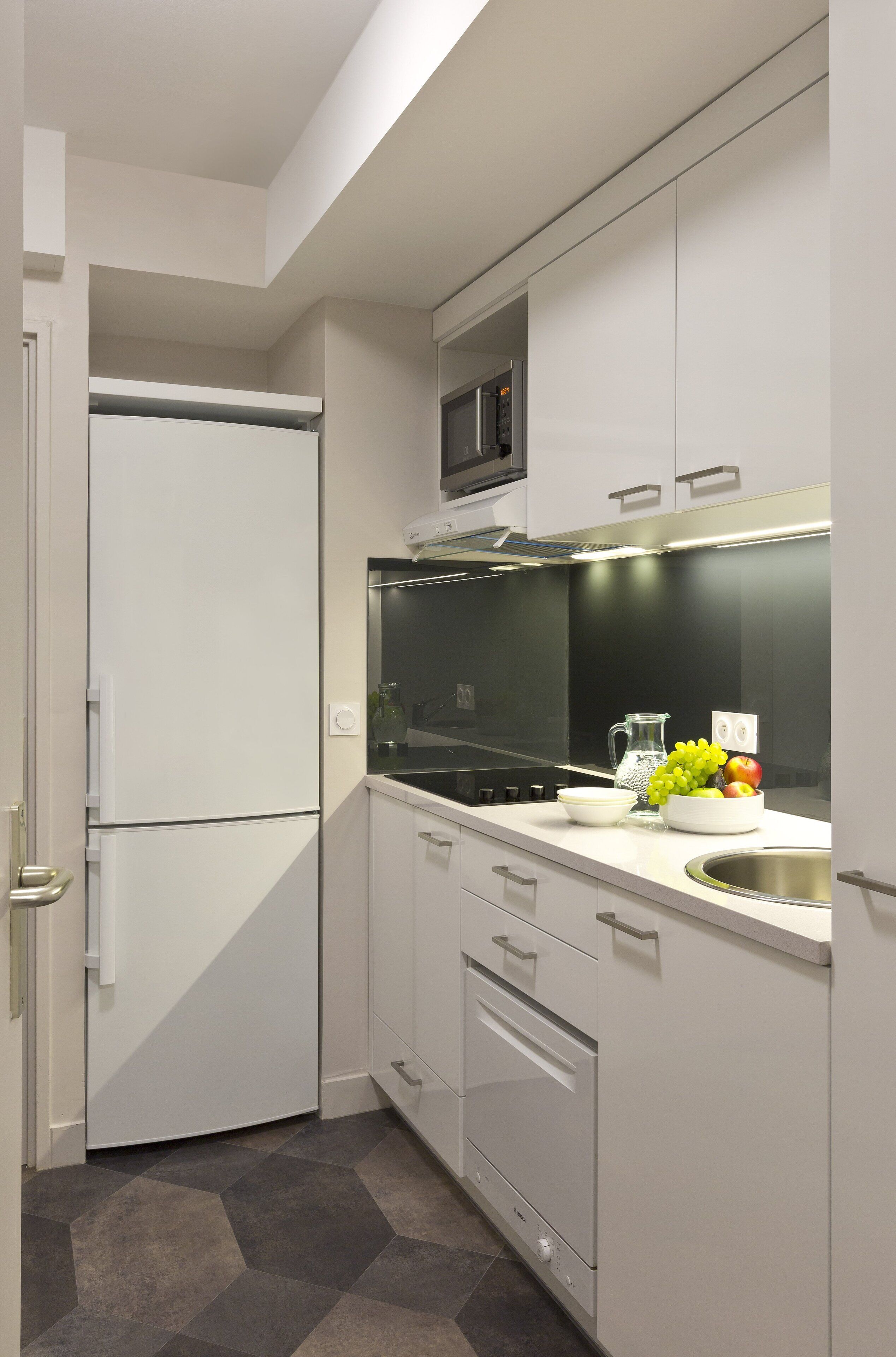 A modern kitchen with white cabinetry, a built-in microwave, a stainless steel sink, and a tiled backsplash.