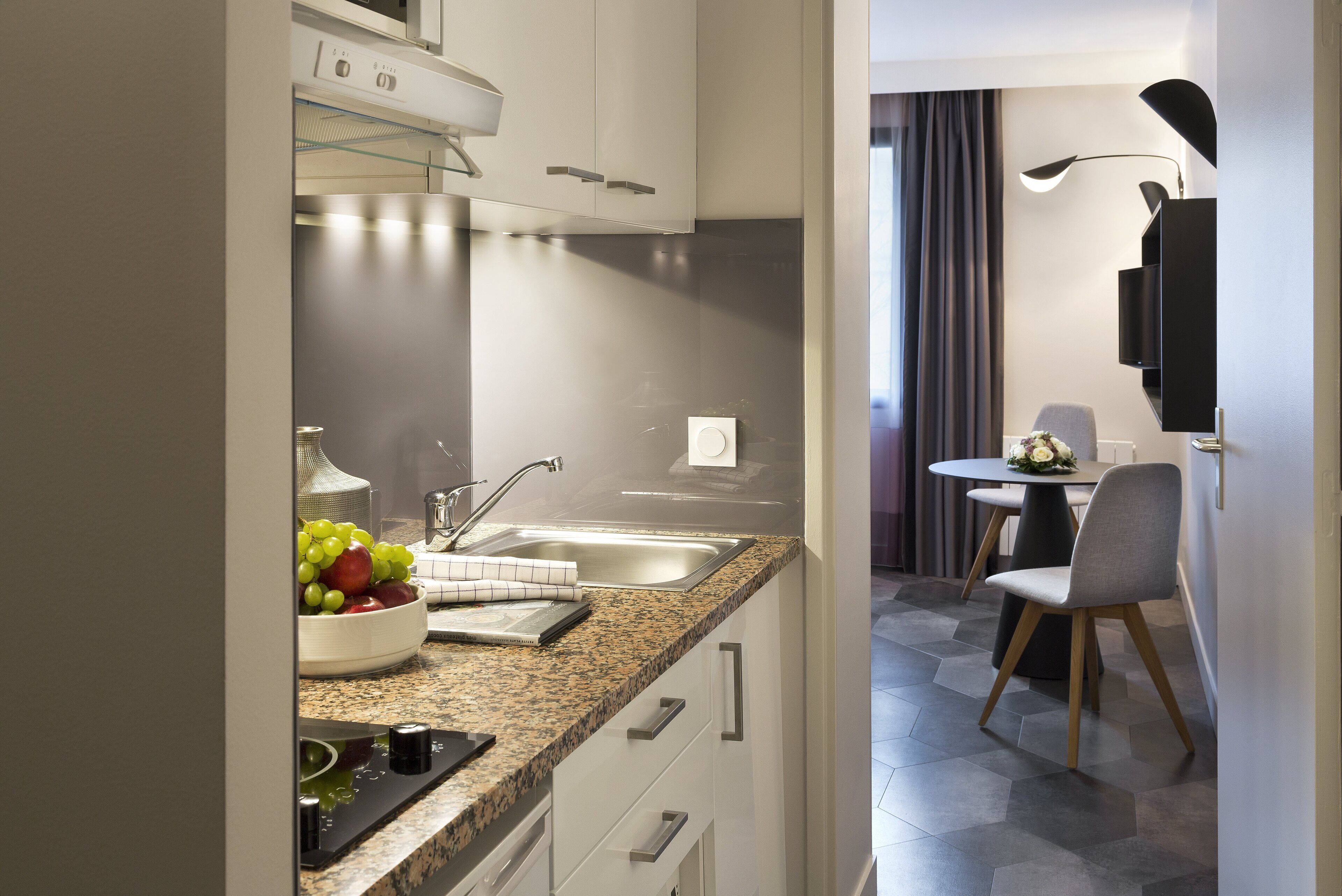 A modern kitchen with granite countertops, a built-in oven, and a dining area with a table and chairs.
