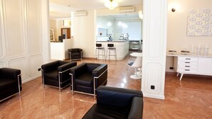 En moderne hotellobby med sorte lædersofaer, et hvidt receptionistskrivebord og et køkkenområde i baggrunden.