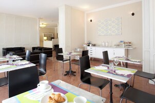 Un'area pranzo con tavoli e sedie, una cucina sullo sfondo e un muro con un motivo decorativo.