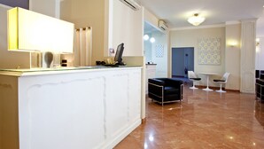 En moderne hotellobby med reception, siddeområde med bord og stole, samt en dekorativ væg med et mønster.