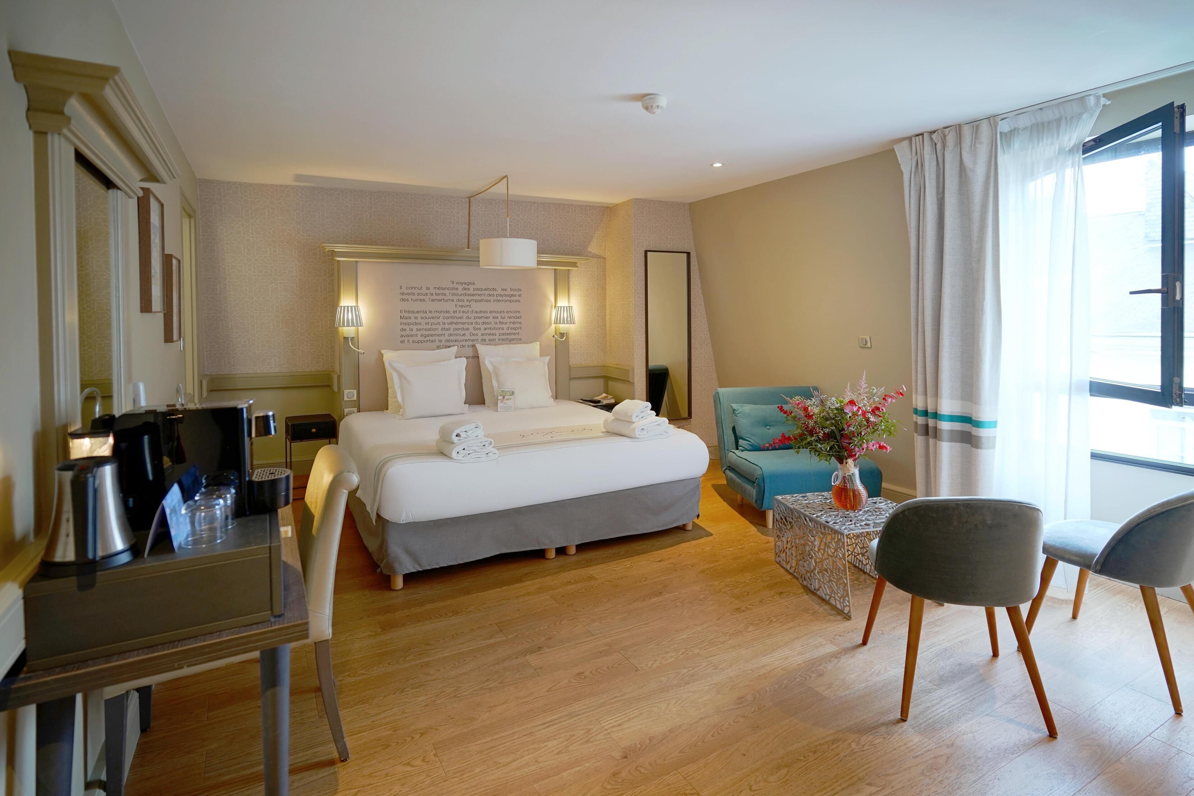 A hotel room with a bed, bedside table, lamp, chair, and a small table with a vase of flowers.