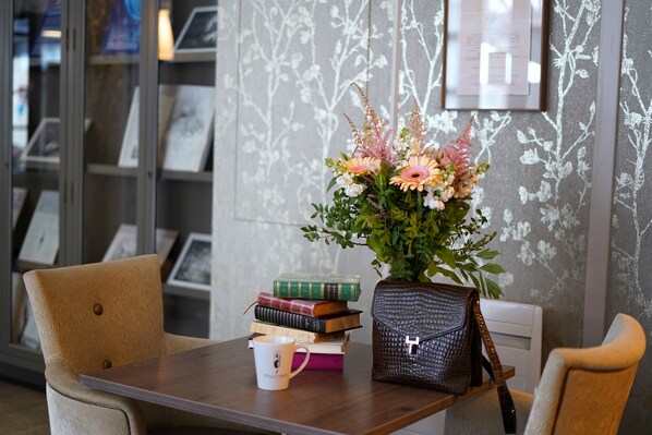 A wooden table with a vase of flowers, a mug, and a stack of books.