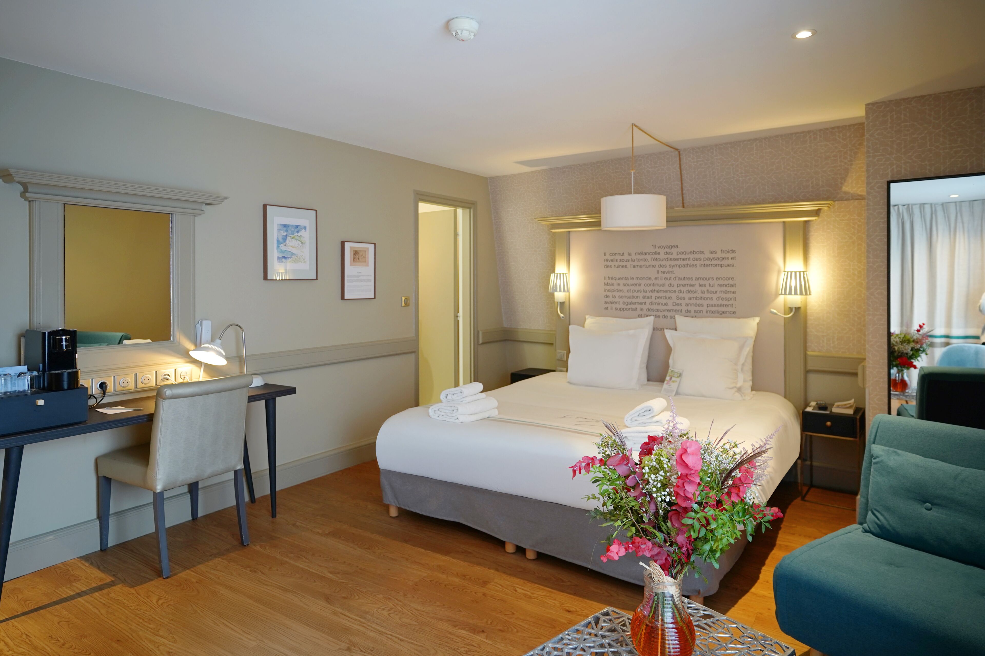 Una habitación de hotel con cama, escritorio, silla y un florero con flores.