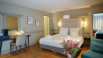 Una habitación de hotel con cama, escritorio, silla y un florero con flores.