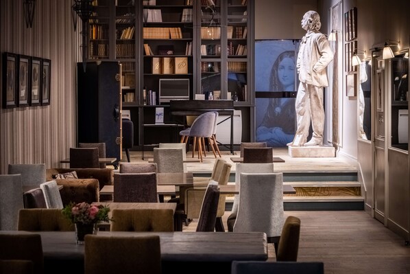 Relax in a sophisticated space with a central statue, comfortable seating, and a bookshelf filled with books and decorative items.