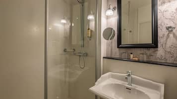 A modern bathroom with a glass-enclosed shower, a white sink, and a mirror with a decorative frame.