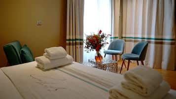 A hotel room with a bed, two chairs, a small table with a vase of flowers, and a window with curtains.