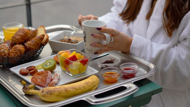 Een dienblad met ontbijtartikelen, waaronder croissants, een banaan en een kom fruit.
