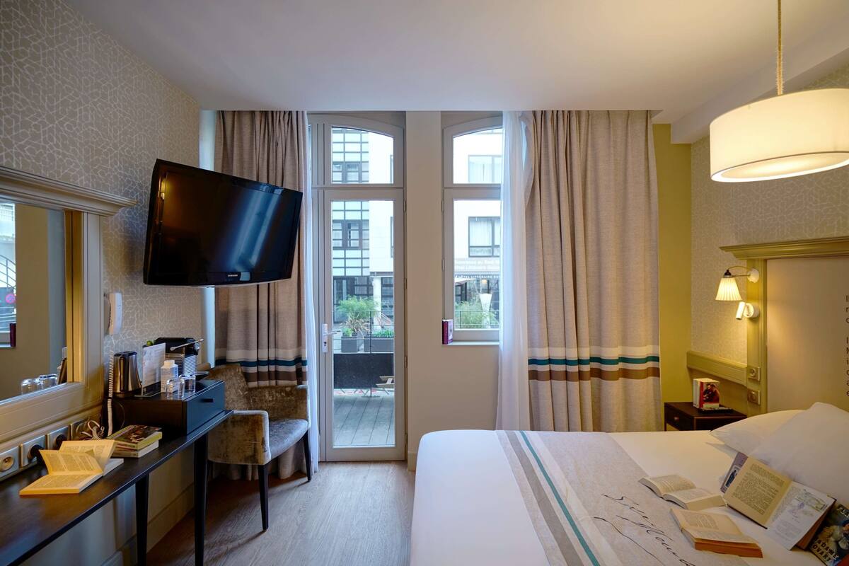 Une chambre d’hôtel comprenant un lit, un bureau avec un téléviseur à écran plat, une chaise et une fenêtre avec des rideaux.