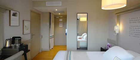 A hotel room with a bed, bedside table, lamp, and a mirror.