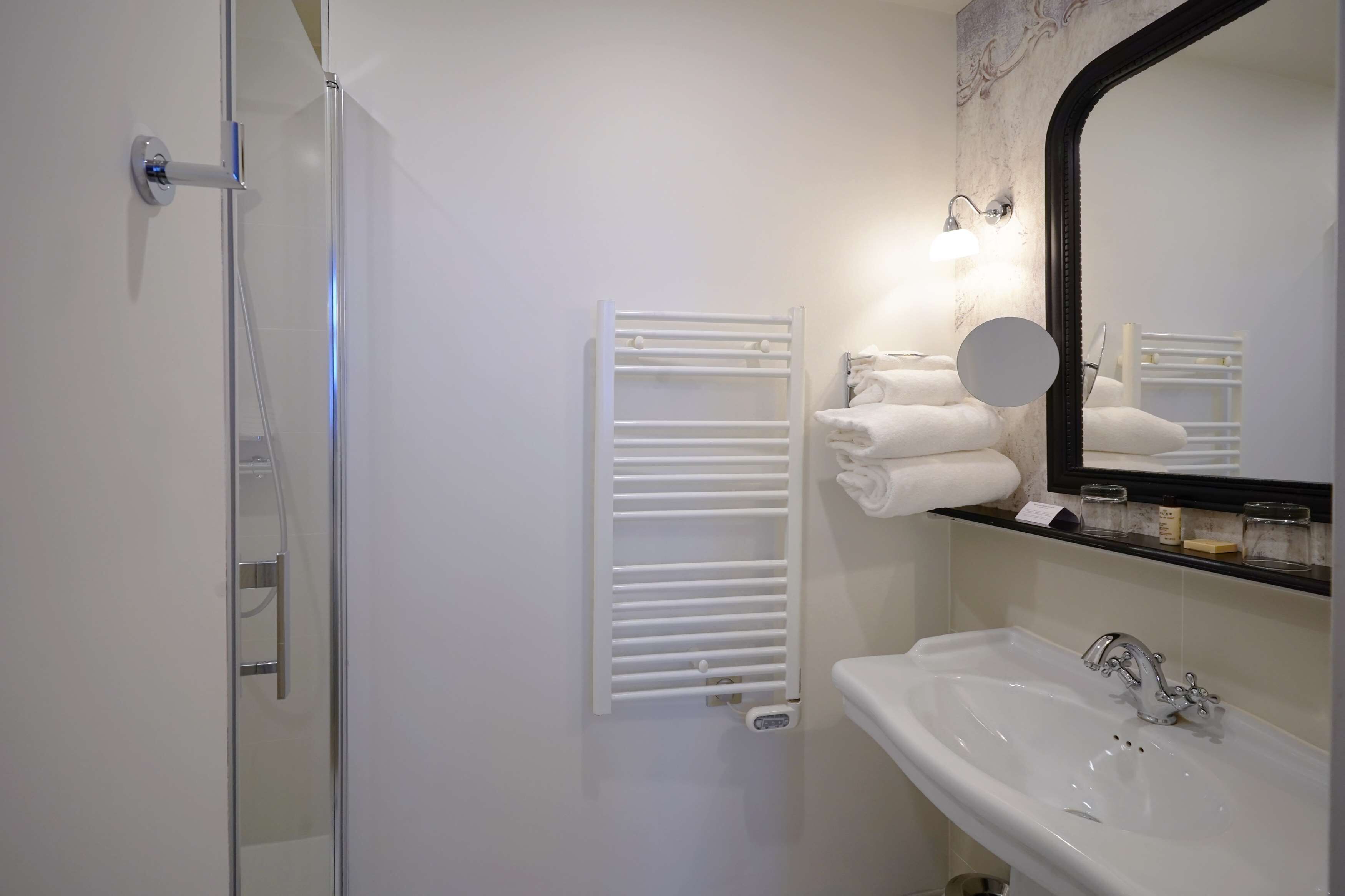 A bathroom with a glass shower enclosure, a white sink with a mirror, and a towel rack with folded towels.