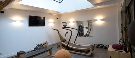 A modern home gym with a ceiling skylight, exercise equipment, and a mirrored wall.