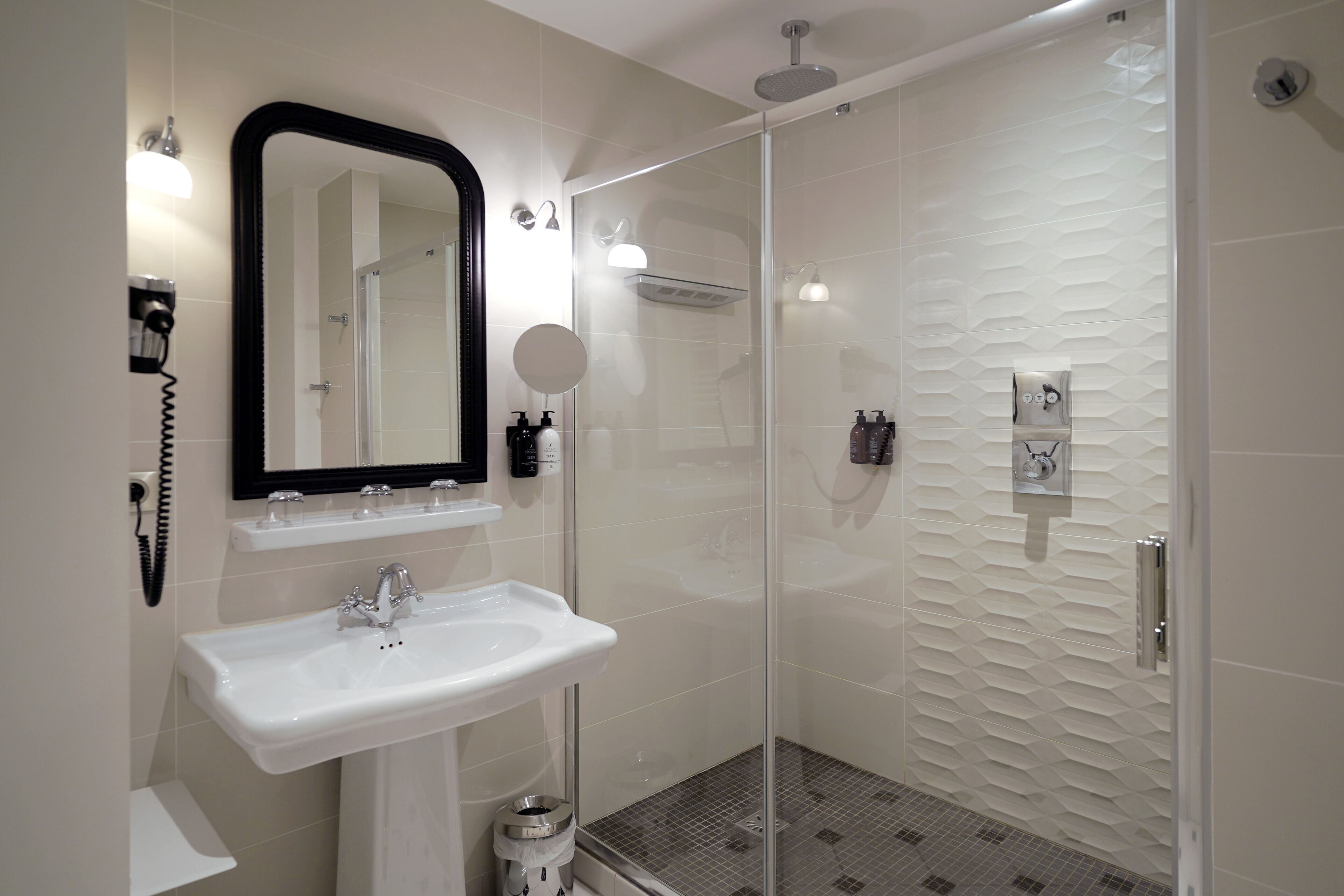 A modern bathroom with a glass-enclosed shower, a white sink, and a mirror above it.