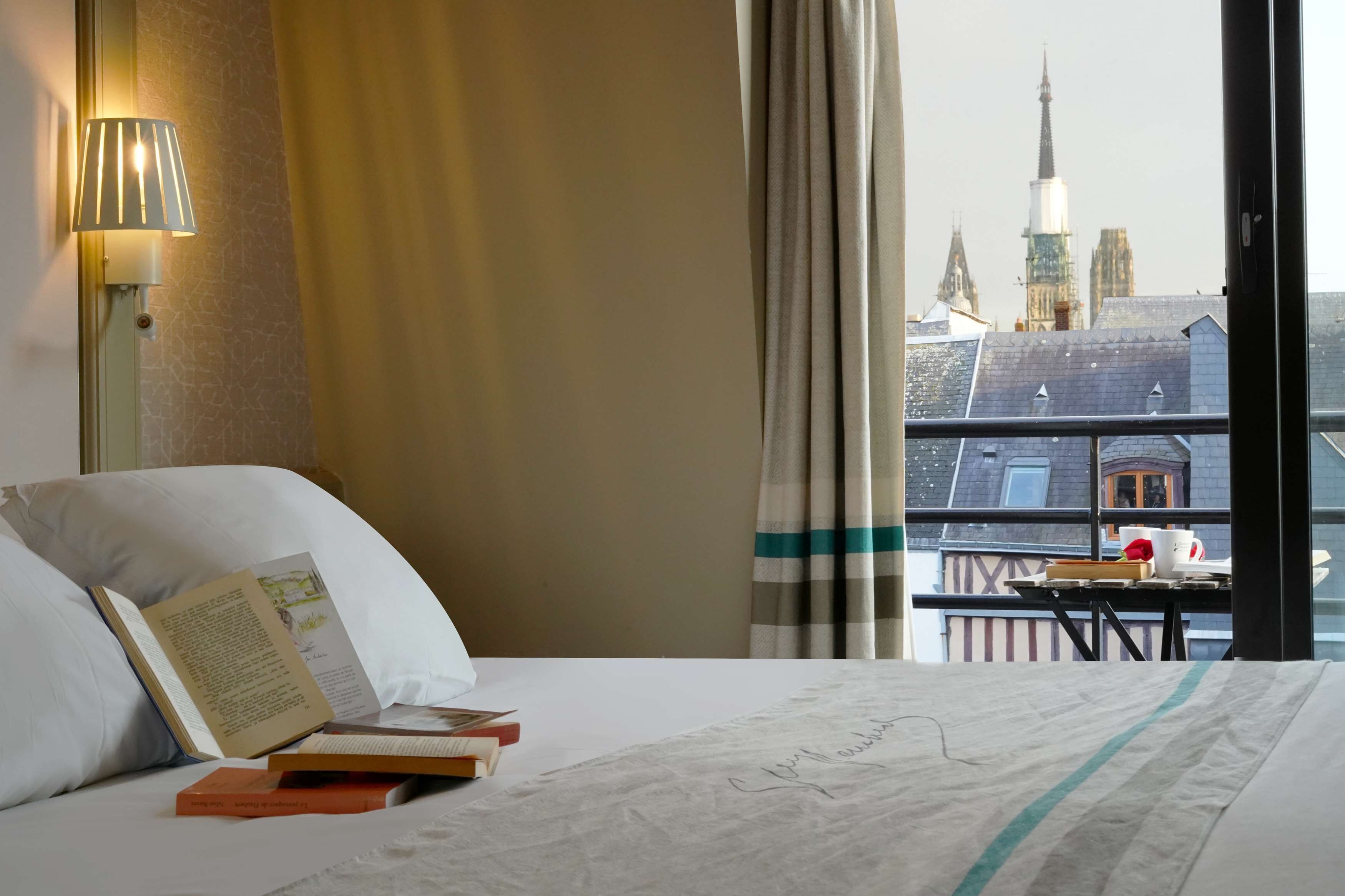 Une chambre d’hôtel avec un lit, une lampe, une fenêtre avec des rideaux et une vue sur des immeubles.