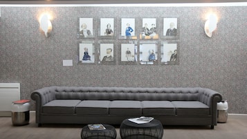 A modern living room with a grey sofa, two black round tables, and a wall with framed pictures.