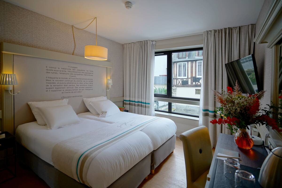 Une chambre d’hôtel avec un grand lit, un bureau avec une chaise, une télévision et une fenêtre avec des rideaux.