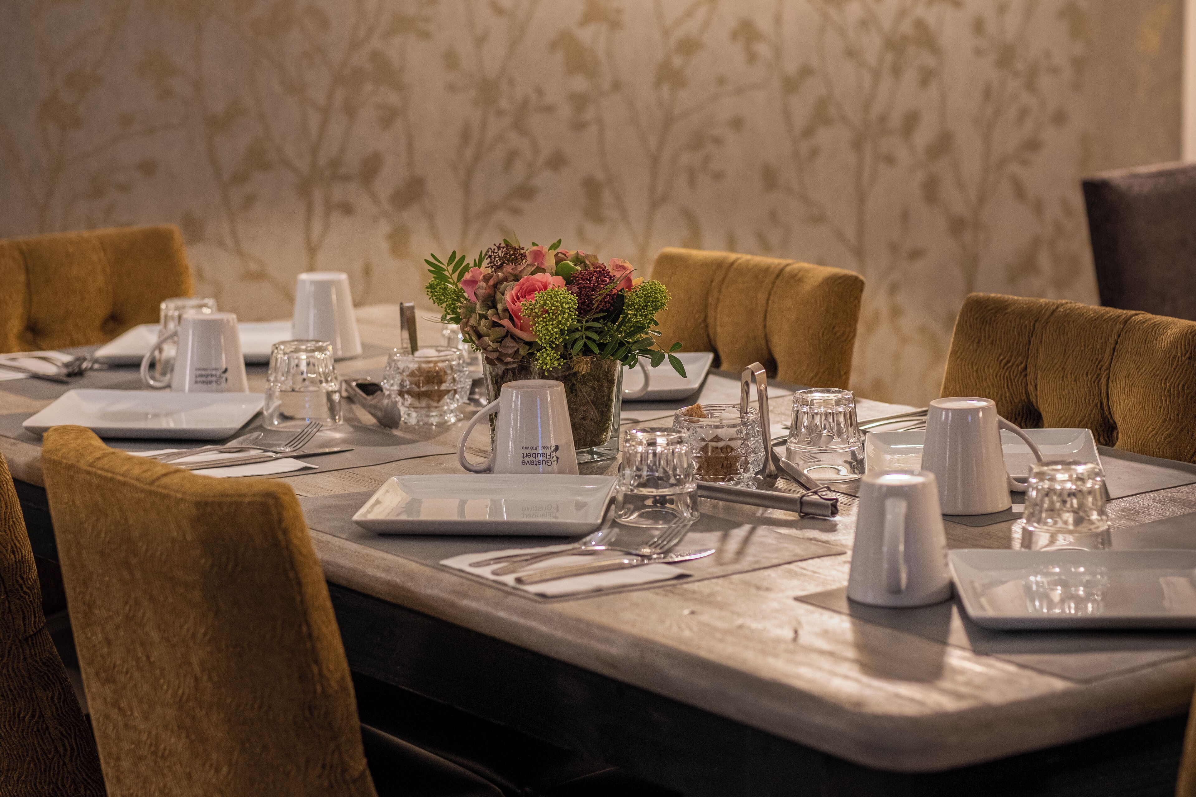 Een gedekte eettafel met borden, bestek, glazen en een bloemenstuk.