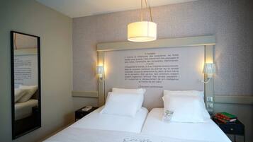 Una habitación de hotel con una cama grande, dos mesitas de noche, un espejo y una pared con una cita enmarcada.