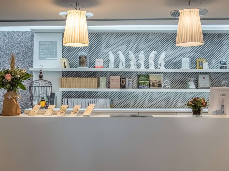 Un área de recepción con un diseño moderno, que incluye una pared con textura, un mostrador de recepción y una variedad de libros y objetos decorativos en estanterías.