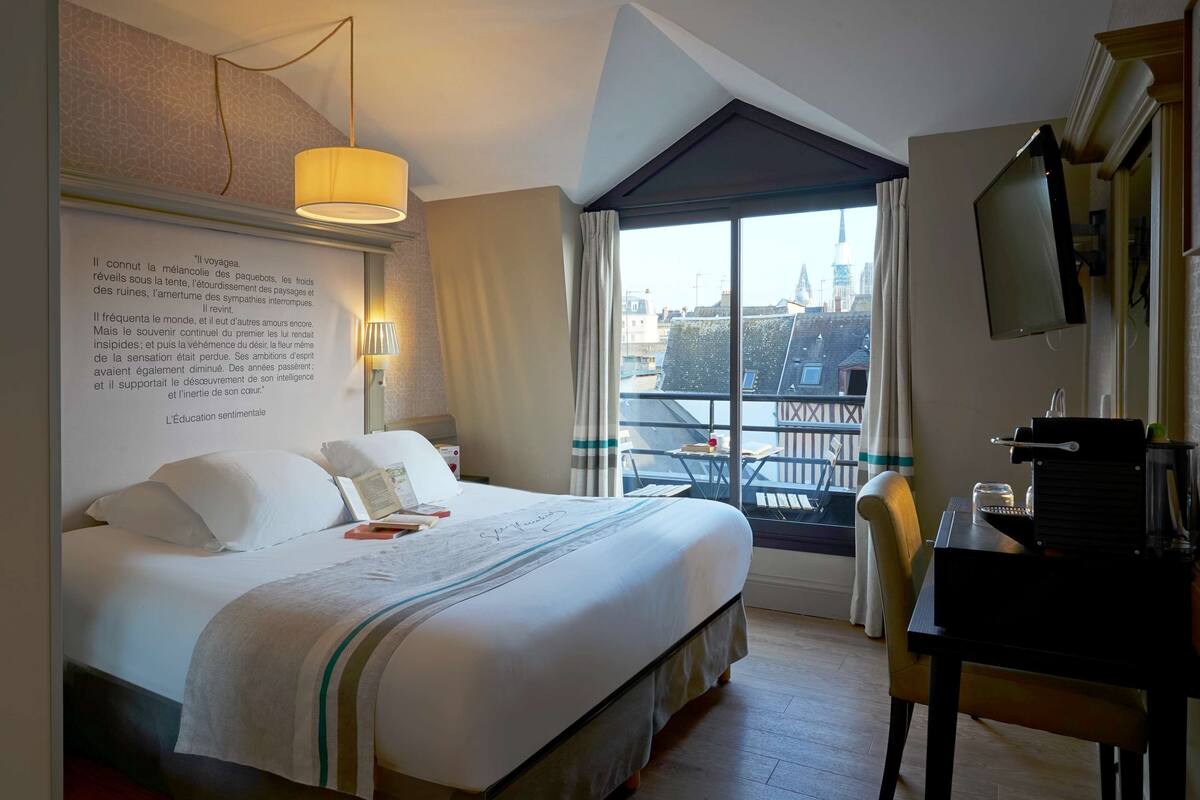 Une chambre d’hôtel avec un grand lit, un bureau avec une machine à café, une télévision et une fenêtre donnant sur des immeubles.