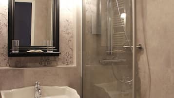 Un baño con lavamanos pedestal, espejo y ducha con mampara de vidrio.