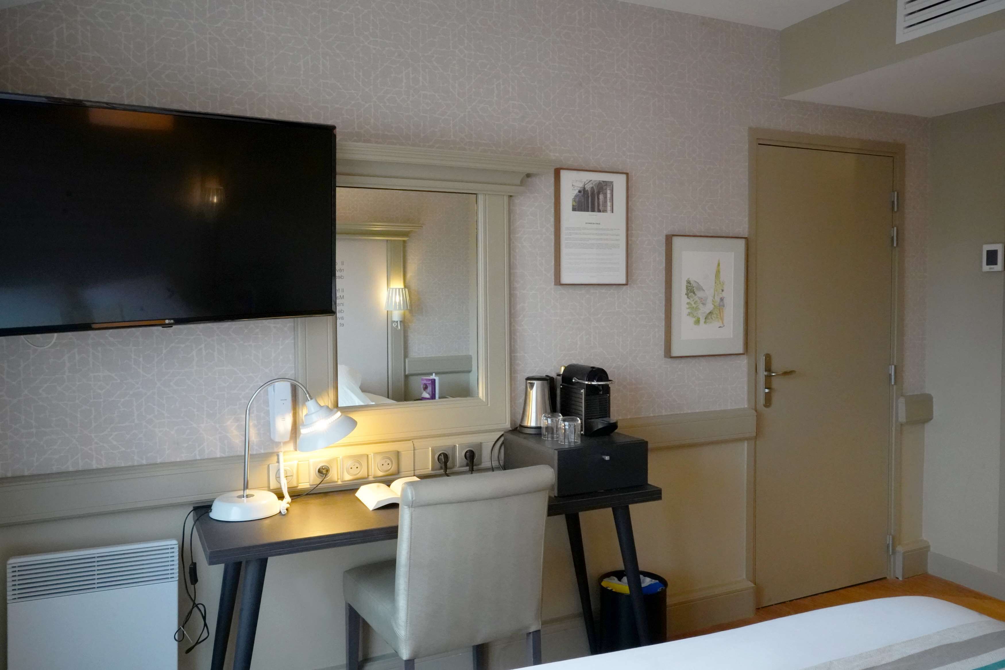 A hotel room with a desk, chair, flat-screen TV, bedside table, and a bed.