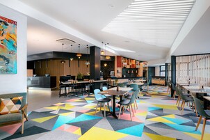 A modern interior with a geometric patterned floor, a reception area, and a dining area with tables and chairs.