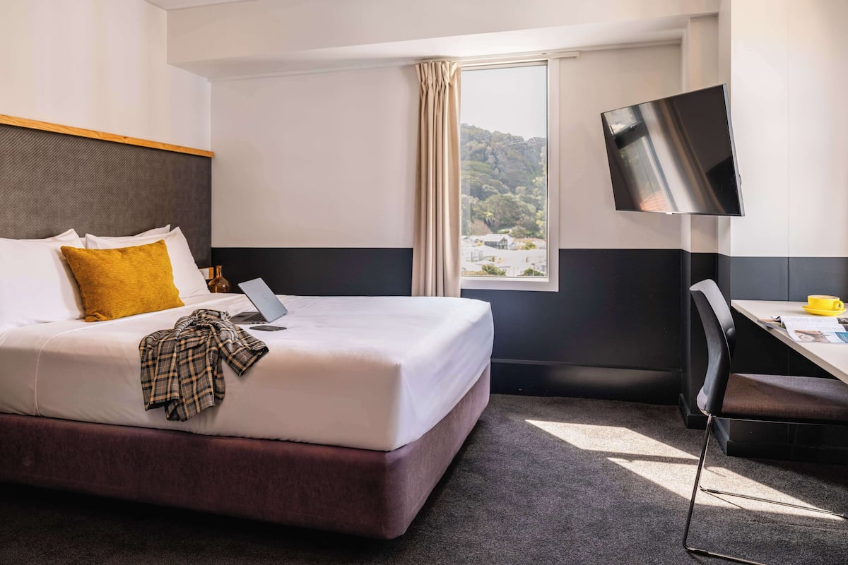 A hotel room with a bed, a desk, a chair, a TV, and a window with a view of a mountain.